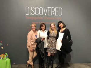 Four women stand in front of a wall that says Discovered: Emerging Artists in Sonoma County